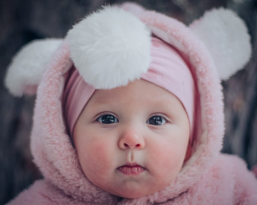 Cute baby in a pink fluffy hoodie with adorable pom pom ears. Close-up portrait.